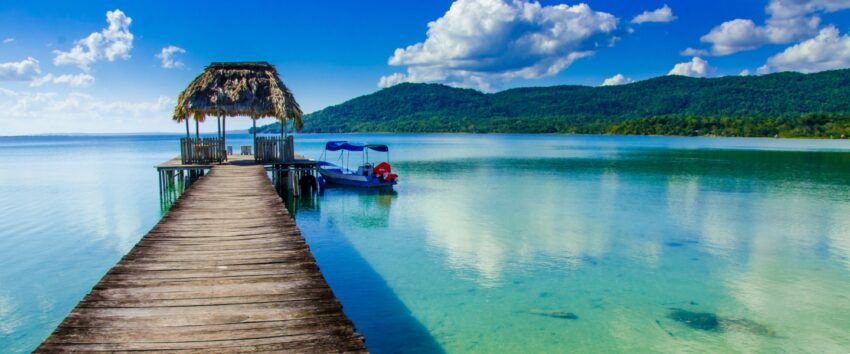 A boat docked next to a wooden dock on turquoise calm ocean
